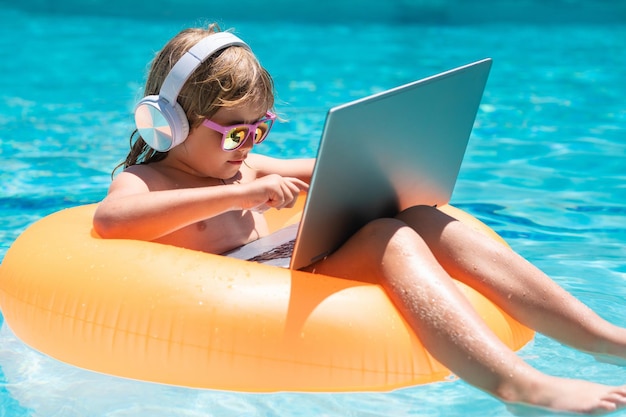 Glücklicher kleiner Junge der Geschäftssommerreise, der Online-Computer-Laptopkind lernt, entspannen sich auf sich hin- und herbewegendem Ring u