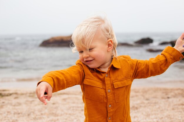 Glücklicher kleiner Junge, der im Herbst auf Sand am Strand sitzt