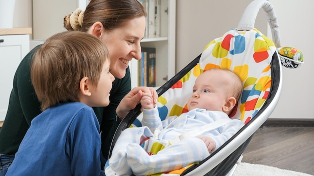 Foto glücklicher kleiner junge, der im stuhl neben seiner familie im wohnzimmer schaukelt. entwicklung des kindes