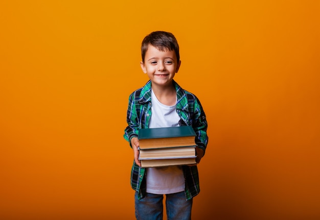 Glücklicher kleiner Junge, der schwere Bücher lokalisierte gelben Hintergrund hält. Bildungskonzept