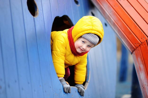 Glücklicher kleiner Junge, der Spaß auf Spielplatz im Freien hat. Aktivurlaub im Frühling und Herbst für Kinder.