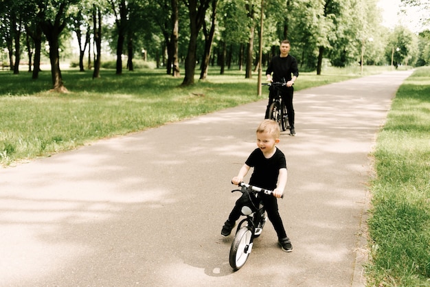 Glücklicher kleiner Junge fährt Fahrrad mit einem jungen Vater im Park