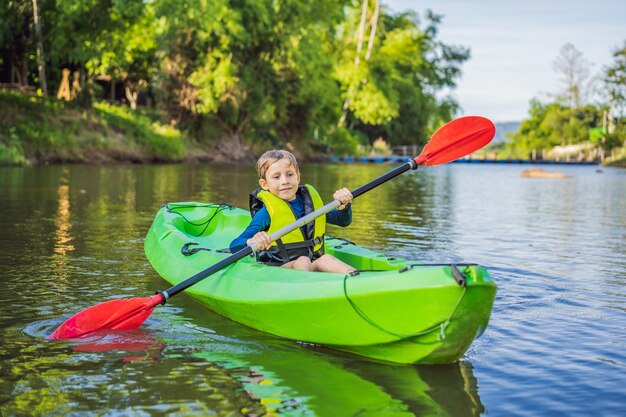 Glücklicher kleiner Junge hält Paddel in einem Kajak auf dem Fluss und genießt einen schönen Sommertag