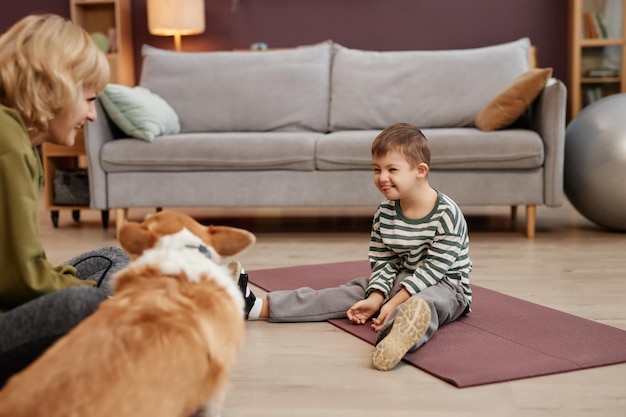 Glücklicher kleiner Junge mit Down-Syndrom, der zu Hause auf dem Boden sitzt