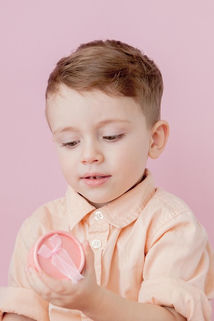 Glücklicher kleiner Junge mit einem Geschenk Foto isoliert auf rosa Hintergrund Lächelnder Junge hält Geschenkbox Konzept von Feiertagen und Geburtstag