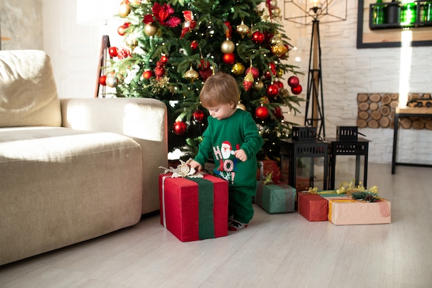 Glücklicher kleiner lächelnder Junge, der mit Weihnachtsgeschenkboxen spielt