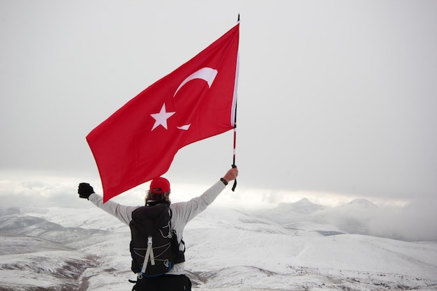 Glücklicher Kletterer auf dem Gipfel Türkische Flagge in der Hand