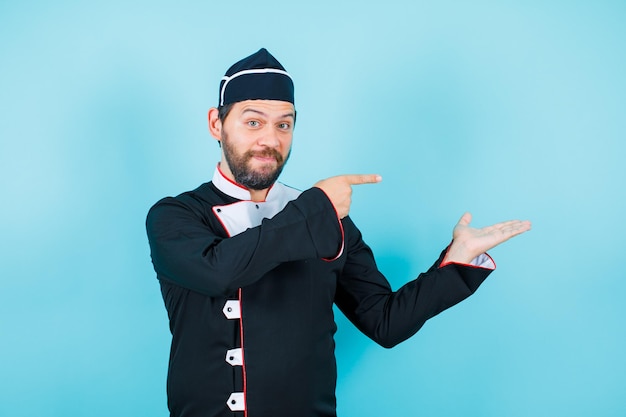 Glücklicher Koch zeigt mit dem Zeigefinger auf blauem Hintergrund nach rechts