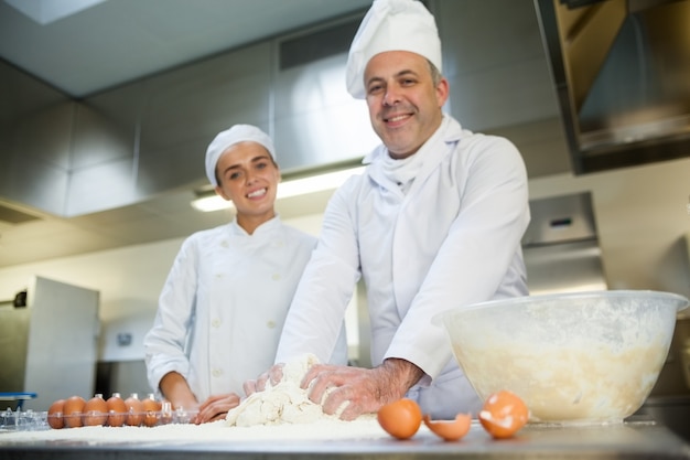 Glücklicher Küchenchef, der lächelnden Auszubildenden zeigt, wie man Teig vorbereitet