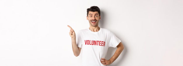 Foto glücklicher lächelnder freiwilliger, der mit dem finger nach links auf den kopierbereich zeigt, der den weißen hintergrund der ankündigung zeigt
