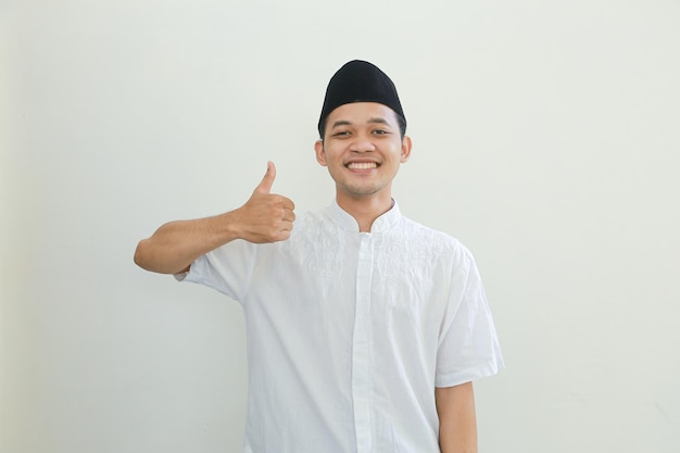 Glücklicher lächelnder hübscher junger asiatischer moslemischer Mann, der Daumen nach oben Geste zeigt