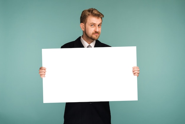 Glücklicher lächelnder junger Geschäftsmann, der leeres Schild auf Blau zeigt