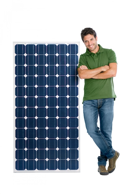 Glücklicher lächelnder junger Mann, der mit einem Solarpanel für erneuerbare Energie steht, lokalisiert auf weißem Hintergrund