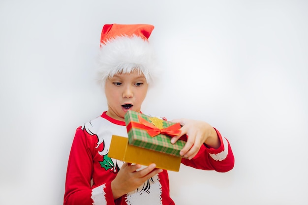 Glücklicher lächelnder kaukasischer Junge im Sankt-T-Shirt und im Hut, der eine Kiste mit Weihnachtsgeschenk öffnet