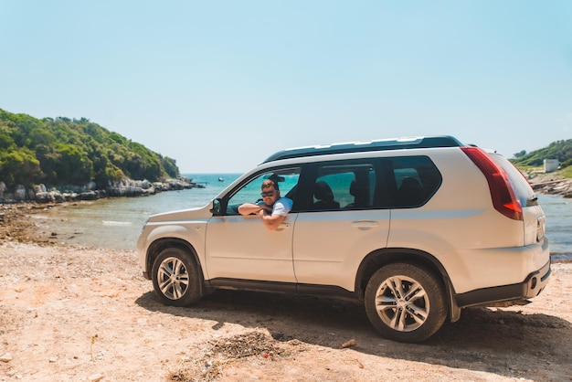 Glücklicher lächelnder Mann, der in der Sommerzeit am Meer im Auto sitzt