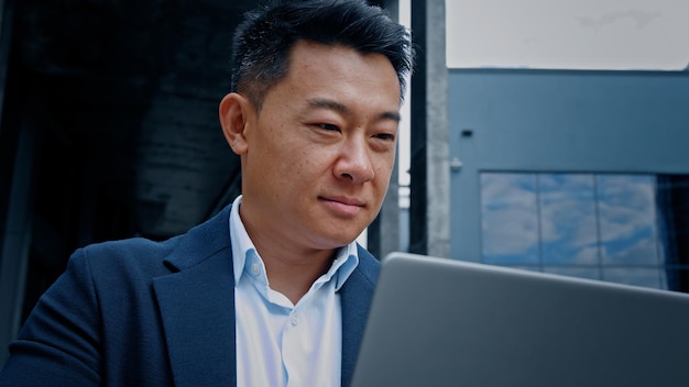 Glücklicher lächelnder Mann Koreanischer chinesischer Geschäftsmann mittleren Alters der 40er Jahre mit Laptop im Freien in der Stadt