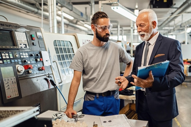 Glücklicher leitender Unternehmensleiter, der mit jungen Arbeitern spricht, während er eine Industrieanlage besucht