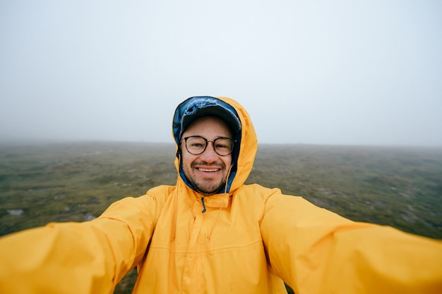 Glücklicher lustiger reisender Mann, der selfie im windigen nebligen Feld nimmt.