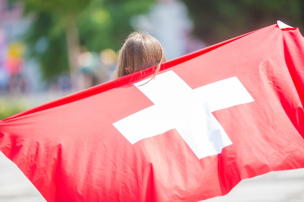 Glücklicher Mädchentourist, der mit der Schweiz-Flagge auf der Straße geht.