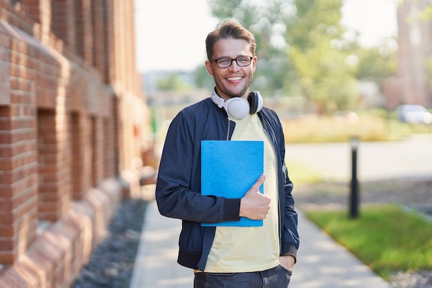 glücklicher männlicher Student auf dem Campus, der im Freien studiert