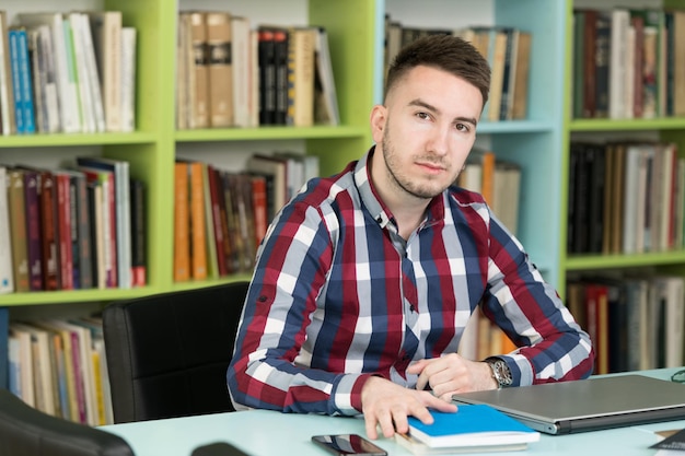 Glücklicher männlicher Student, der mit Laptop in der Bibliothek arbeitet