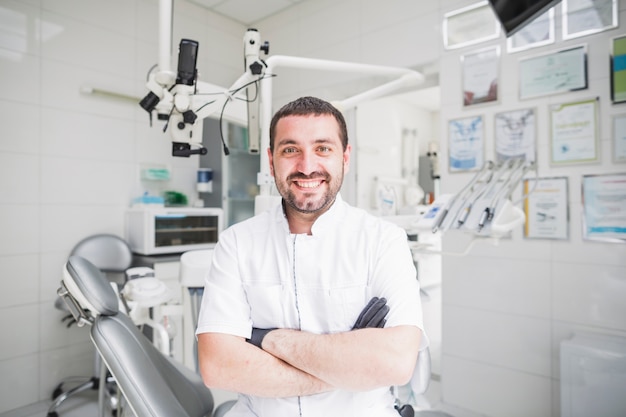 Glücklicher männlicher Zahnarzt mit den gefalteten Händen, die Kamera betrachten