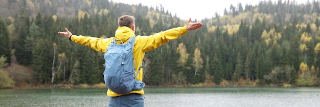 Glücklicher Mann breitet die Hände zur Seite aus und genießt die wilde Natur, während er als Tourist mit Rucksackständern wandert