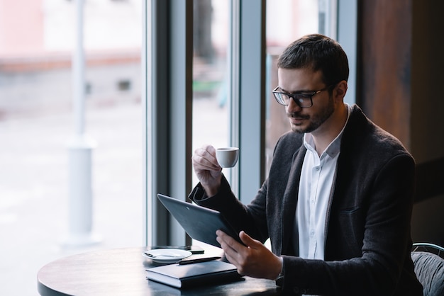 Glücklicher Mann, der am Kaffeetisch sitzt und Tablette benutzt