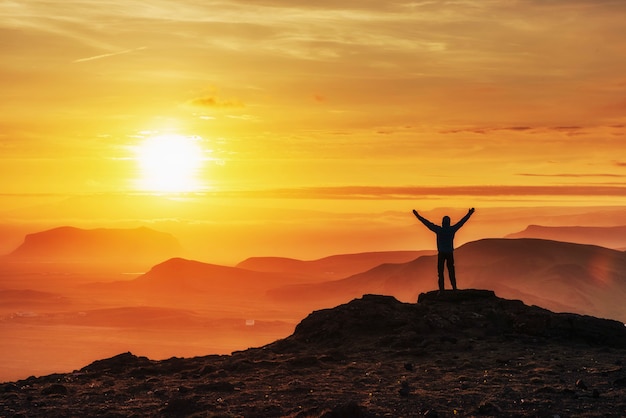 Glücklicher Mann, der auf einer Klippe bei Sonnenuntergang steht