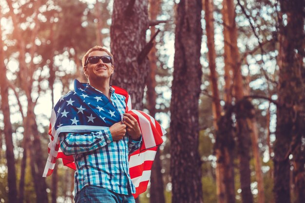 Foto glücklicher mann, der bei sonnenuntergang die usa-flagge im park hält