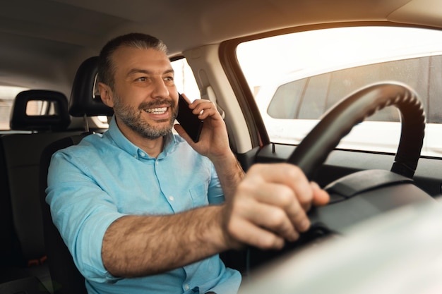 Glücklicher Mann, der beim Autofahren auf dem Smartphone spricht