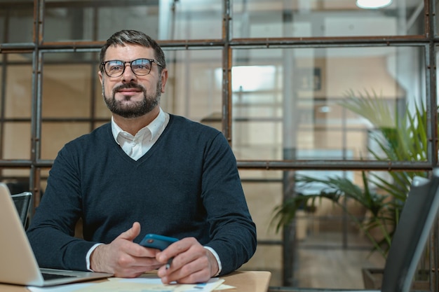 Glücklicher Mann, der eine Brille trägt und lächelt, während er an seinem Laptop arbeitet