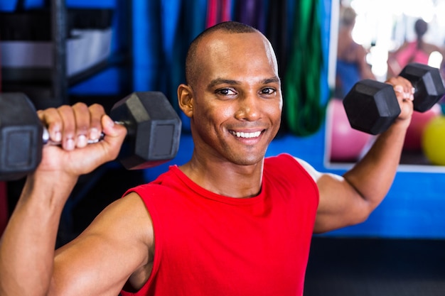 glücklicher Mann, der Hantel im Fitnessstudio hebt