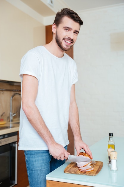 Glücklicher Mann, der in der Küche geräuchertes Fleisch schneidet und nach vorne schaut