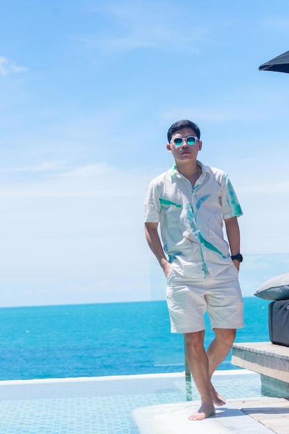 Glücklicher Mann, der in der Nähe des Infinity-Pools im Luxushotel gegen das Meer geht. junge Männer genießen im tropischen Resort. Entspannungs-, Sommer-, Reise-, Ferien-, Ferien- und Wochenendkonzept