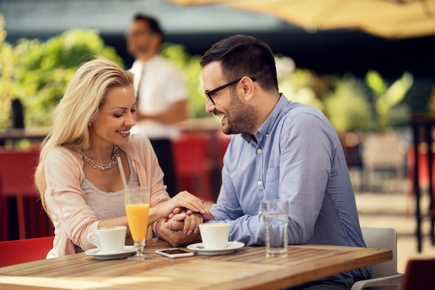 Glücklicher Mann, der mit seiner Freundin Händchen hält und mit ihr spricht, während er in einem Café auf einem Date ist