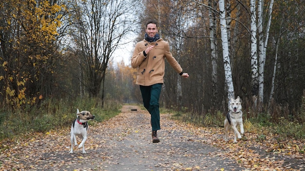 Glücklicher Mann, der mit zwei Hunden draußen in Kamerarichtung läuft