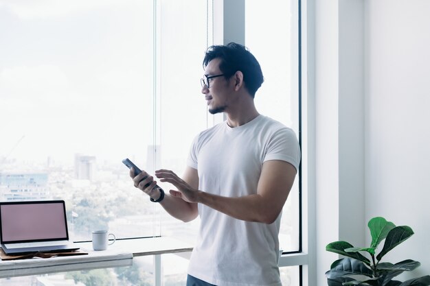 Glücklicher Mann, der Smartphone mit Balkonblickkonzept verwendet, arbeitet von zu Hause aus