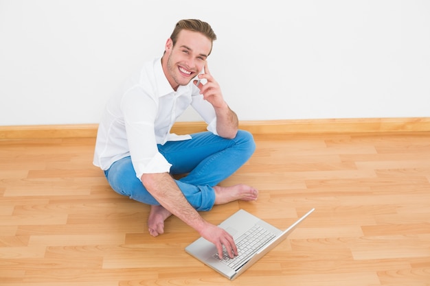 Glücklicher Mann, der zu Hause auf Boden unter Verwendung des Laptops sitzt