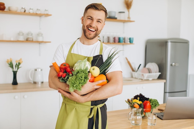 Glücklicher Mann, der zu Hause viele verschiedene frische Gemüsesorten in der Küche hält