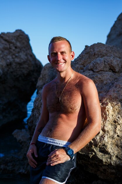 Glücklicher Mann Freude im Urlaub, steht am Ufer und schaut auf das Meer. Herrenshorts, Sonne, Strand