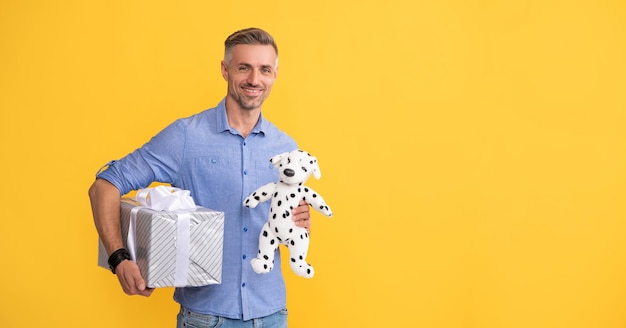Glücklicher Mann hält Geschenkbox und Spielzeug auf gelbem Hintergrund, Kopienraum kaufen