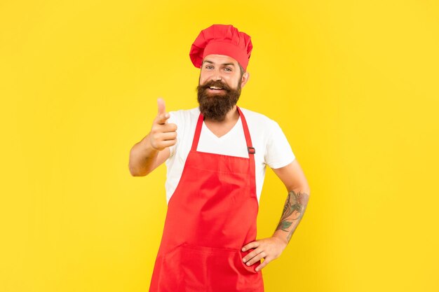 Glücklicher Mann in Toque und Schürze, der mit dem Finger nach vorne zeigt, gelber Hintergrund, Koch.