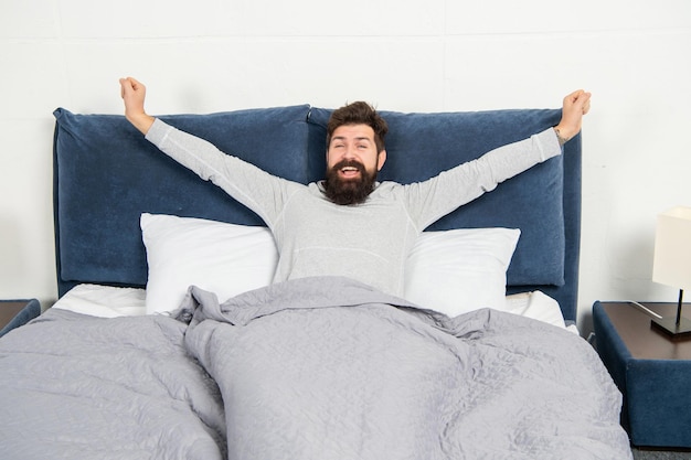 Glücklicher Mann lächelt und streckt sich im Bett und wacht morgens nach dem Schlafen auf