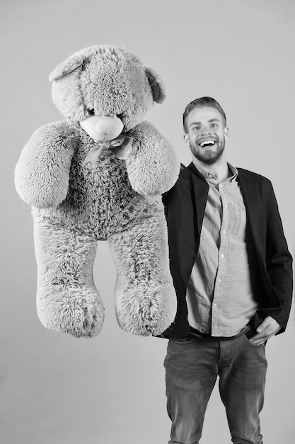 Glücklicher Mann mit grauem Teddybär Macho-Lächeln mit großem Tierspielzeug Geschenk- und Geschenkkonzept Mode und Stil Geburtstag oder Jubiläum und Feiertagsfeier