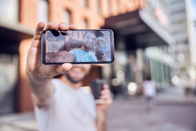 Glücklicher Mann mit Kaffee macht Selfie auf der Straße