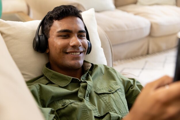 Glücklicher Mann mit Kopfhörern, der auf dem Sofa liegt und zu Hause ein Tablet benutzt