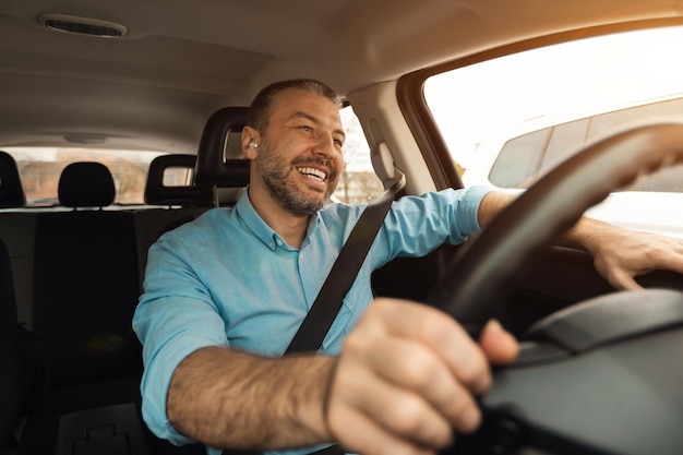 Glücklicher Mann mit Kopfhörern, der Musik beim Fahren eines Luxusautos genießt