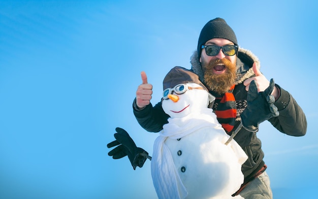 Glücklicher Mann mit Schneemann auf Hintergrund des Winters im Freien Schneemann für Winterfahne