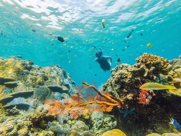 Glücklicher Mann mit Schnorchelmaske taucht unter Wasser mit tropischen Fischen im Korallenriff-Meerespool